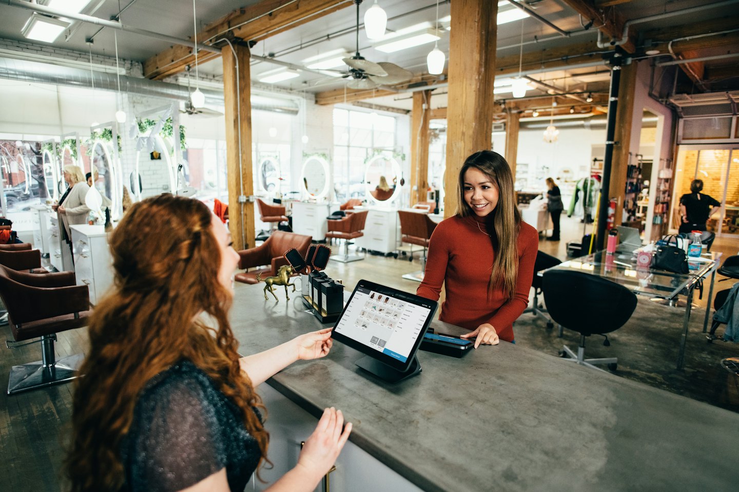 Woman shows customer item selection on tablet at counter.